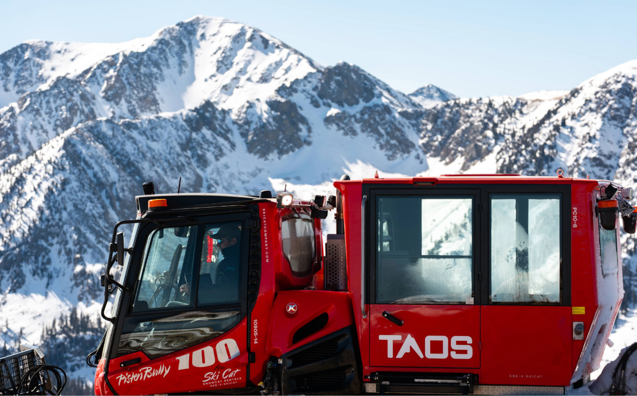 Red Taos Ski Valley snowcat vehicle against snow-covered mountains in Taos, New Mexico