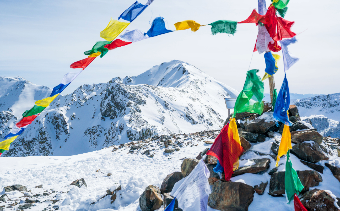Snow-covered mountain peak with colorful prayer flags overlooking a winter landscape in Taos, New Mexico